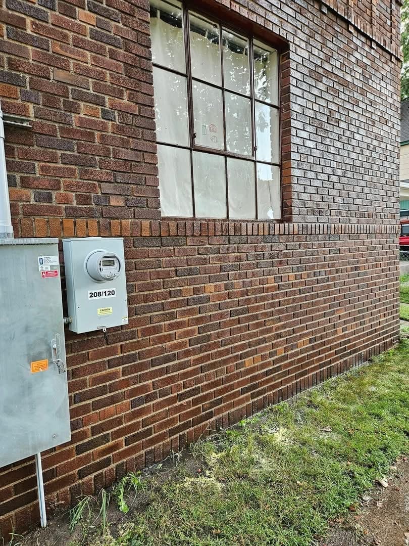 The same brick elevation and meter cabinet after graffiti removal, with clean brick and bare galvanised metal