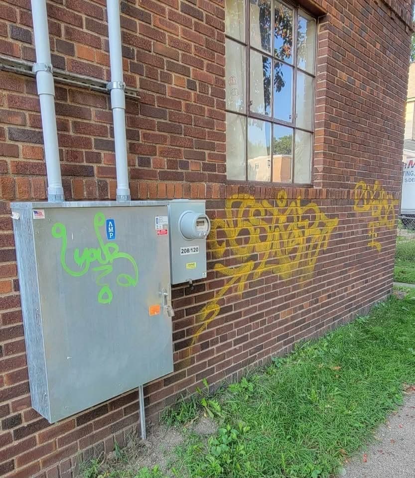 Yellow and green spray tags across brick and a galvanised electrical meter cabinet before removal