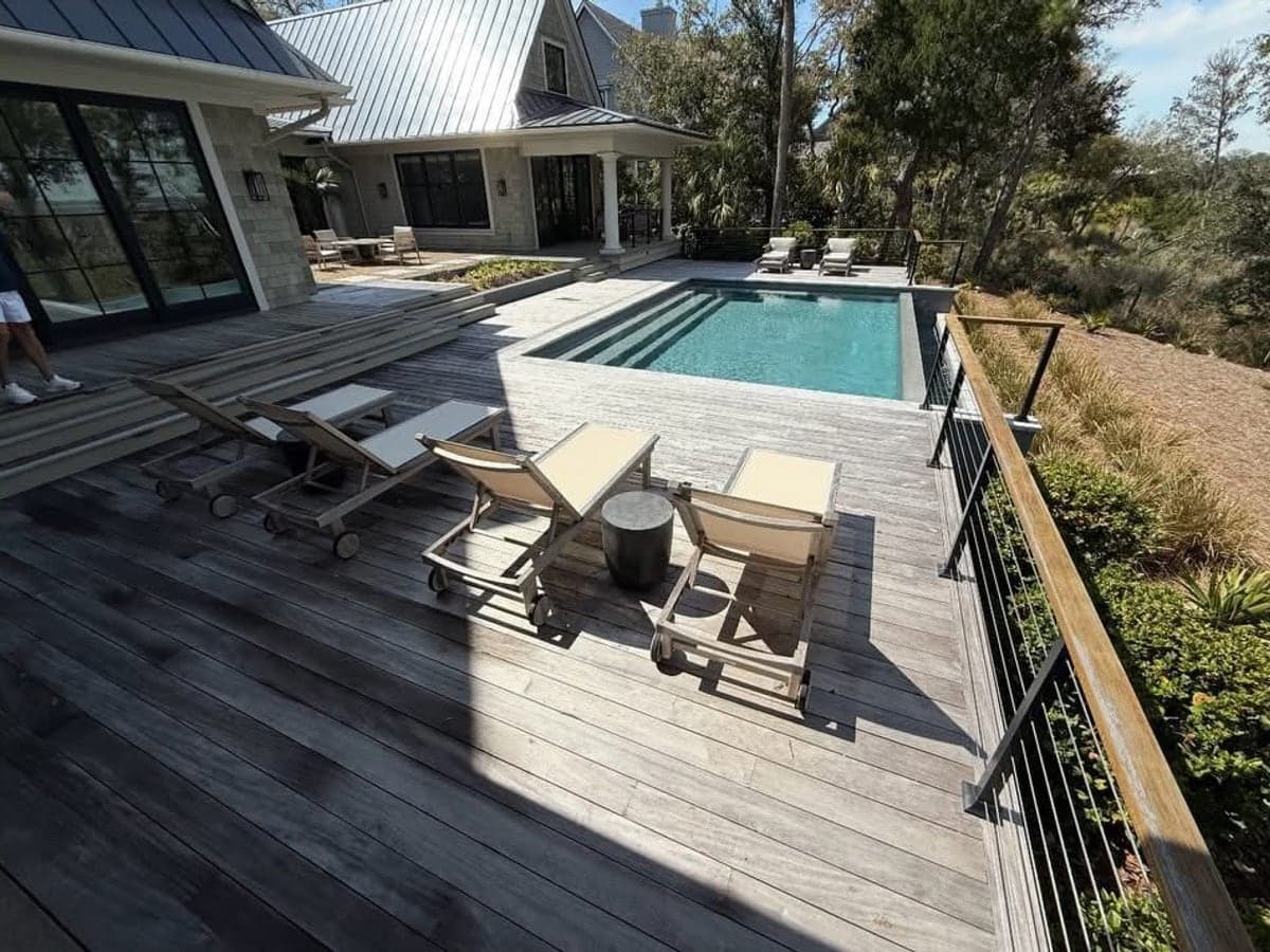 Grey weathered timber pool deck with loungers before cleaning, the boards dull and streaked