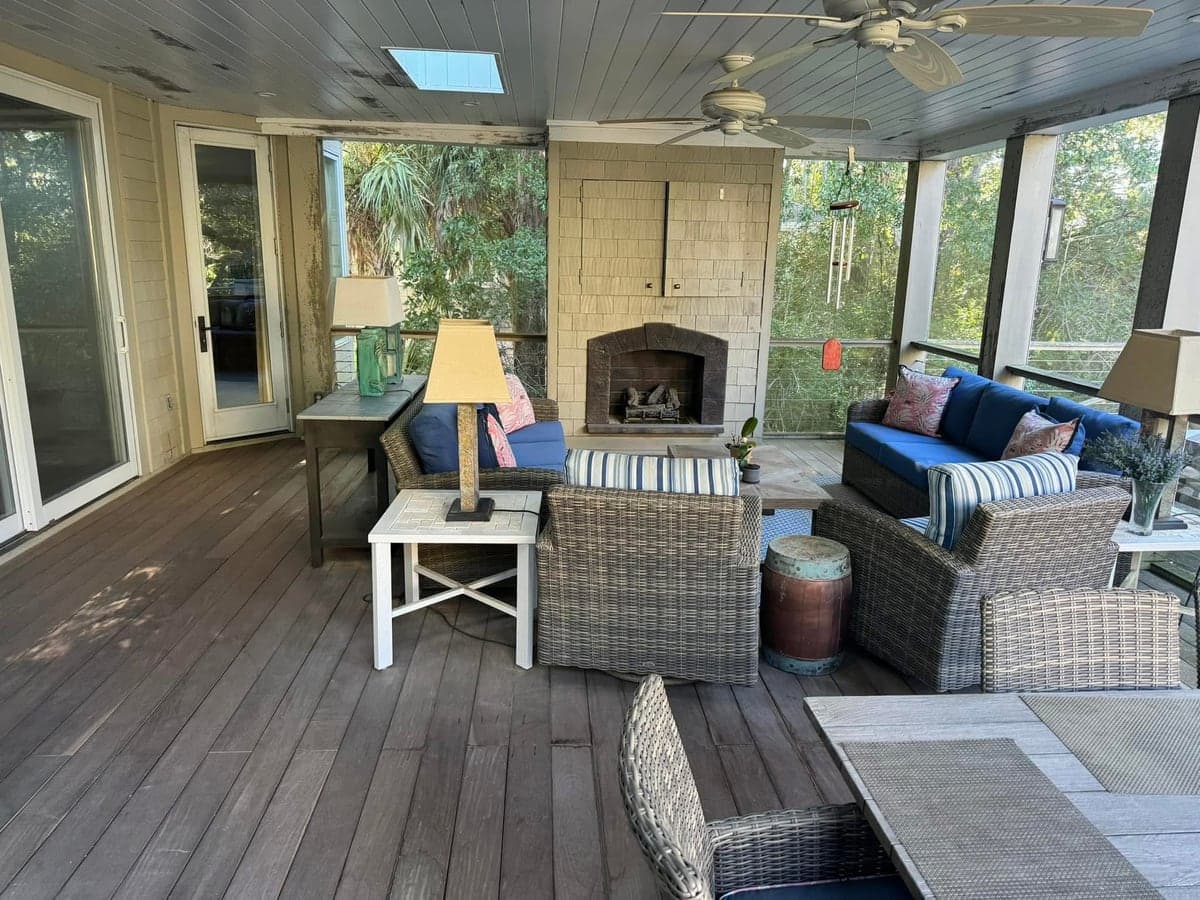 Screened porch with grey dulled decking before cleaning, wicker furniture and a fireplace behind