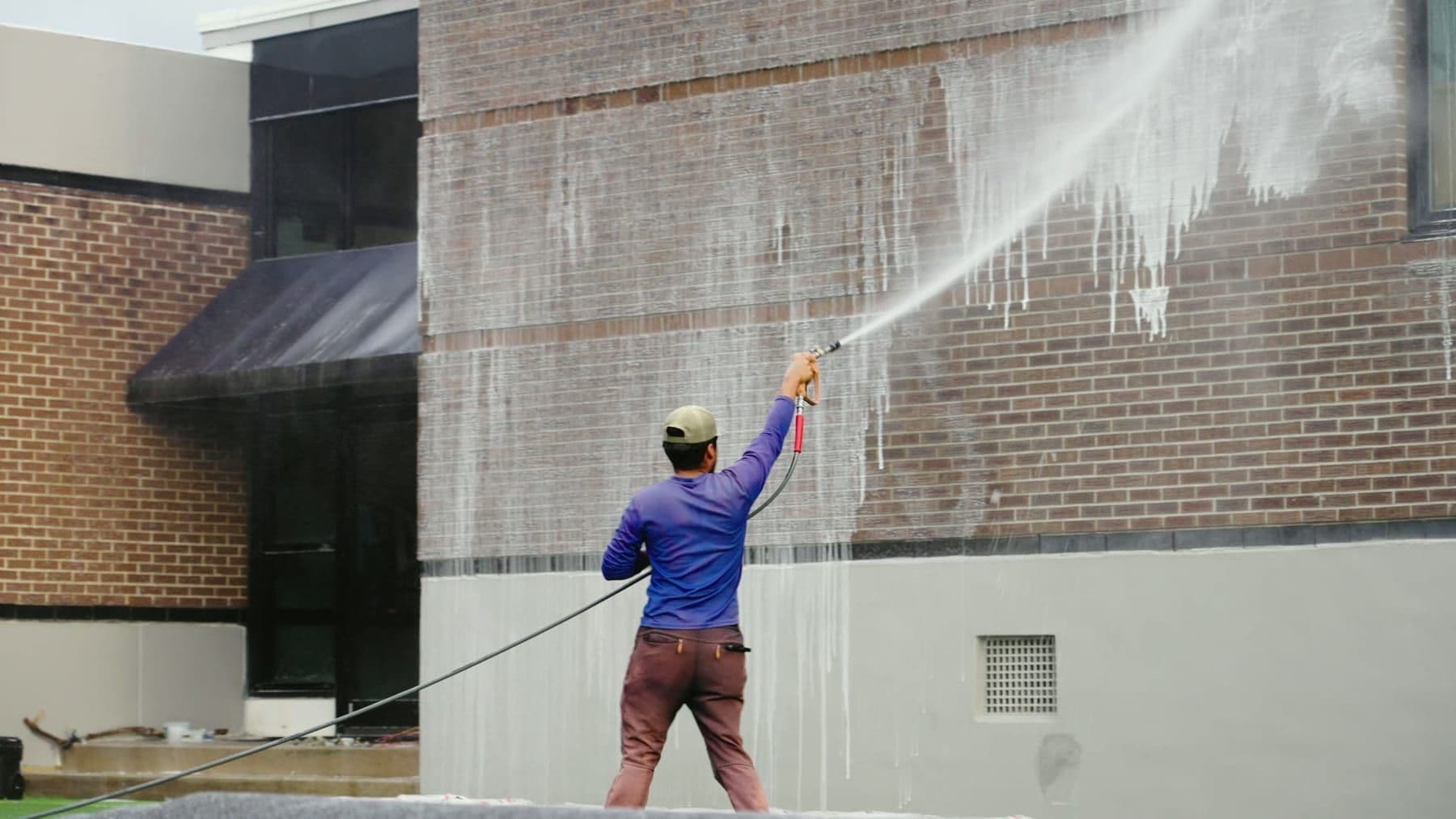A technician soft-washing a commercial brick building from the ground in Charleston, SC
