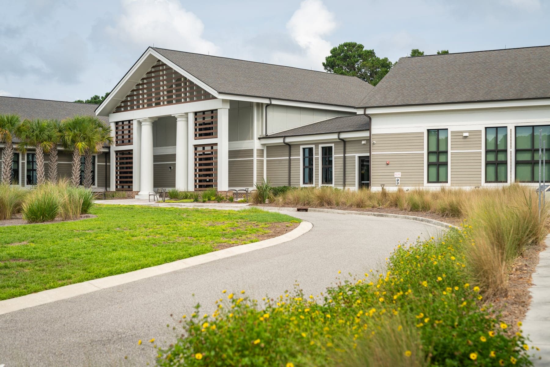 A low-rise professional building with a columned entry portico, lap siding and a curving paved drive edged with native grasses