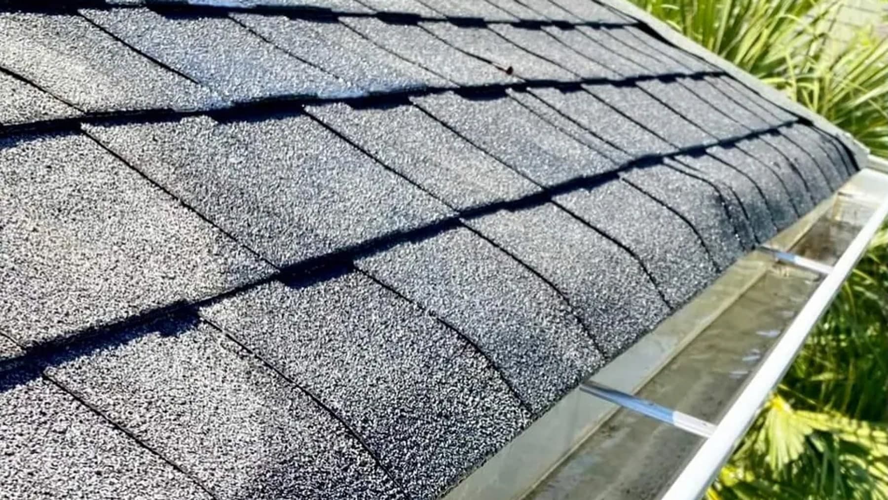 A cleared white gutter running along a shingle roof edge with the trough empty and draining