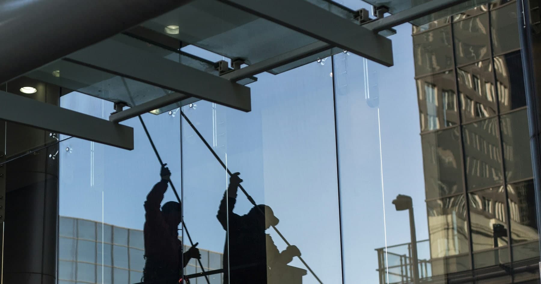 Two technicians cleaning a full-height commercial glass curtain wall with extension poles