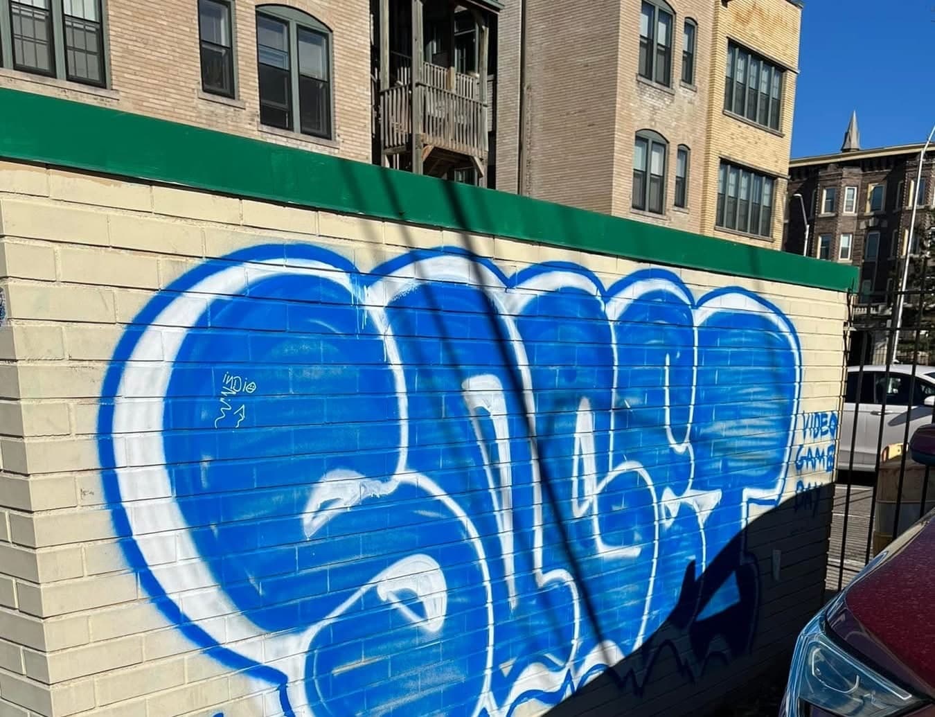 Large blue spray-painted tag covering a commercial block wall, before graffiti removal